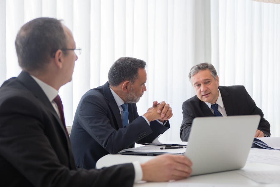 Three businessmen collaborating during a meeting around a laptop in a bright office