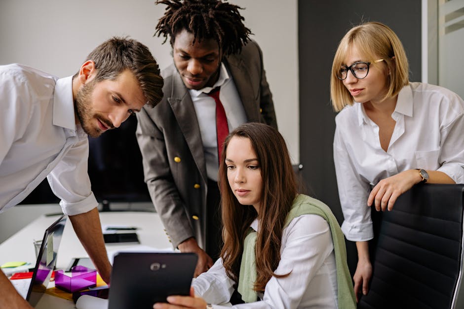 A diverse group of colleagues engaged in team discussion, utilizing a tablet in a modern office setting