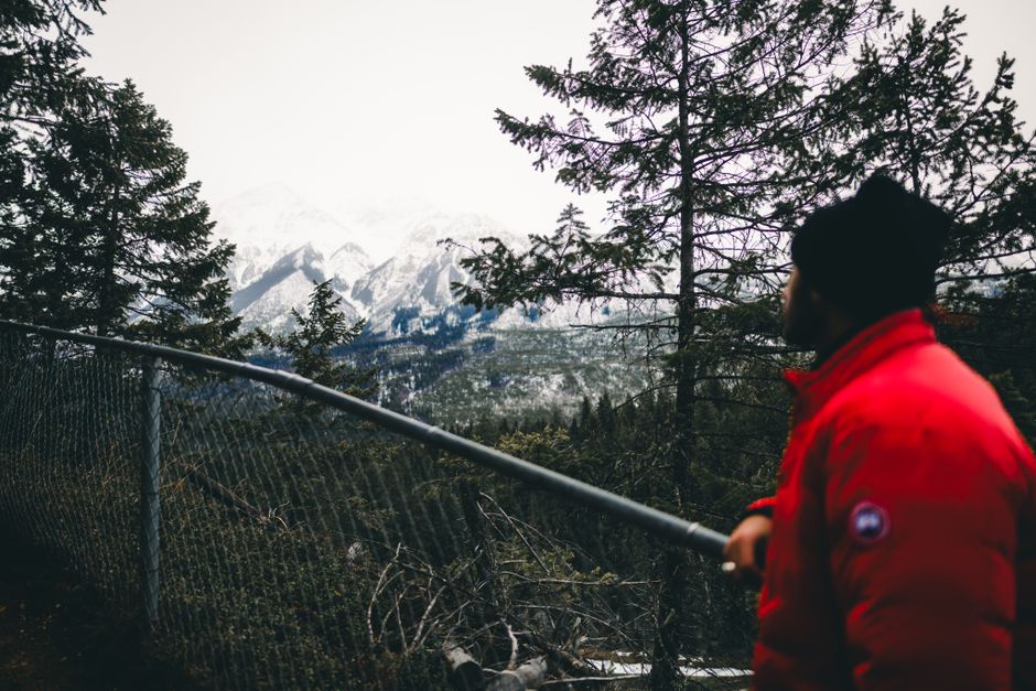 A hiker in a red jacket admires the Canadian Rockies from a forest viewpoint.