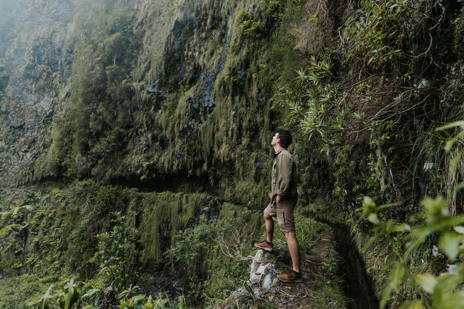 A man explores a moss-covered cliff in Portugal, showcasing adventure and natural beauty.